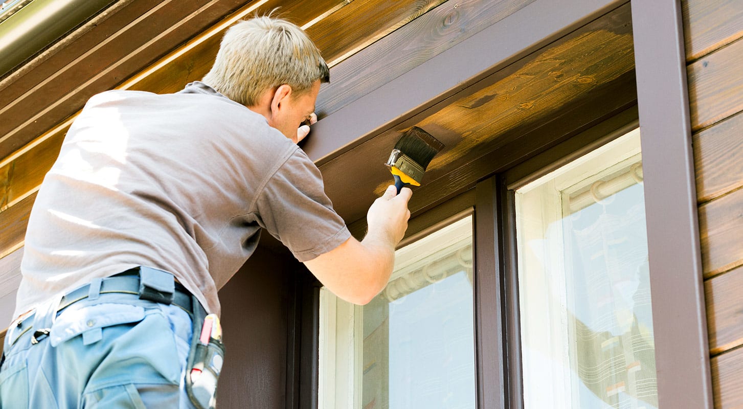 A man paints the window frame of a house.